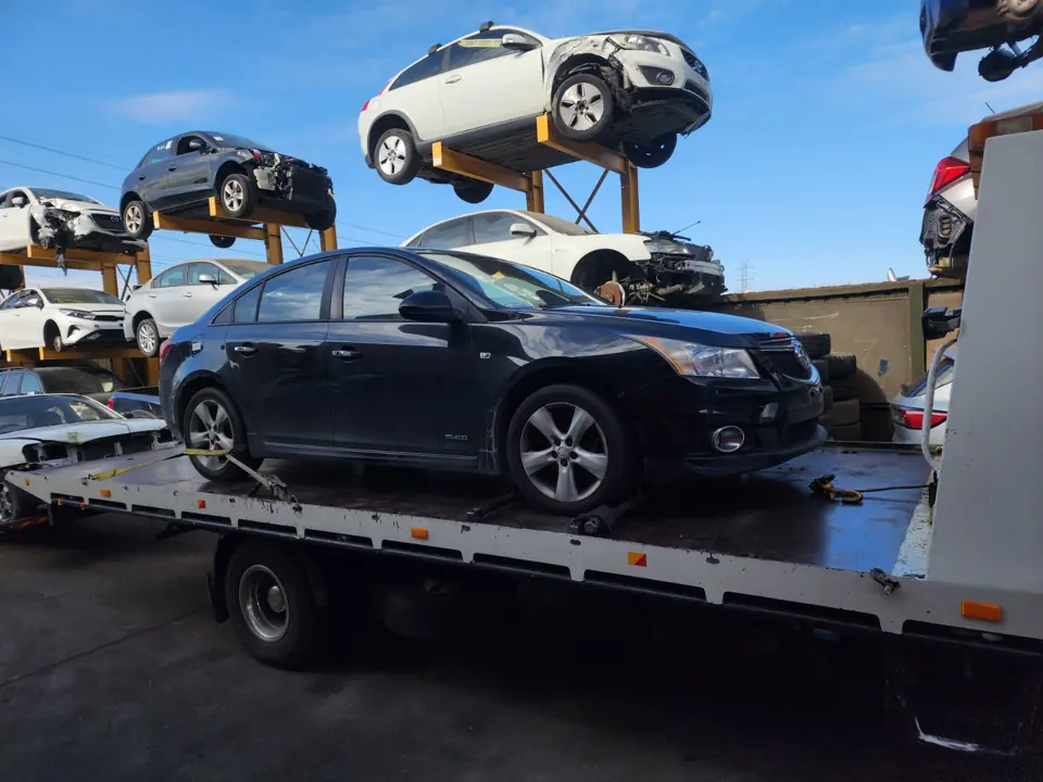 Dark sedan loaded on a flatbed truck in a vehicle yard