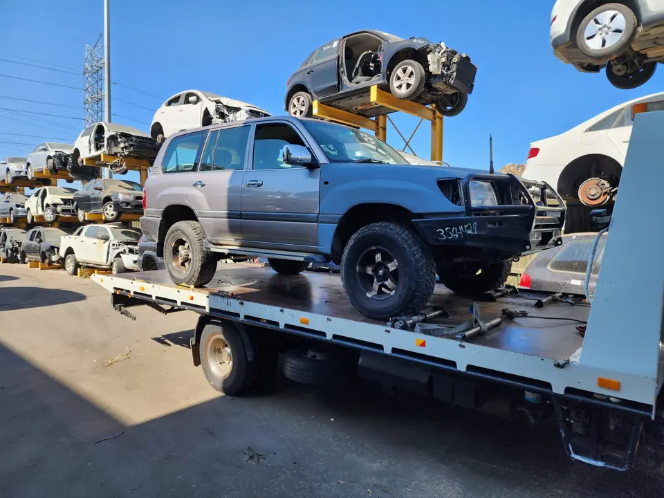 Blue SUV on a flatbed with vehicles stored behind it