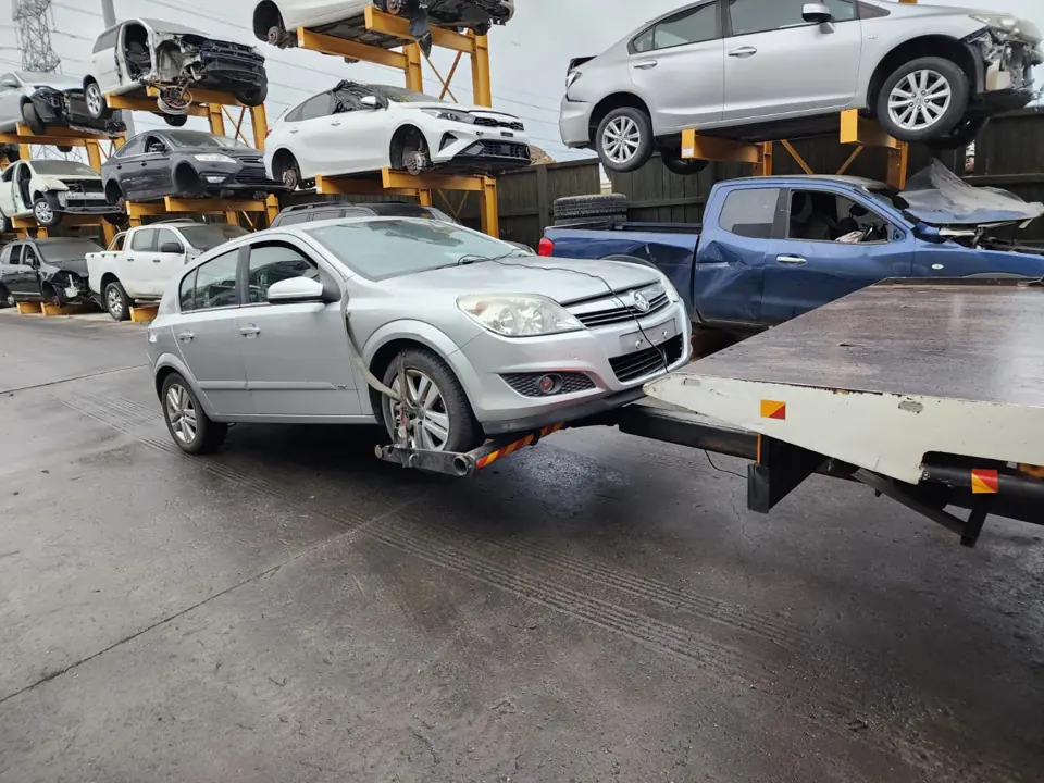 Silver wagon beside stacked vehicles in a yard
