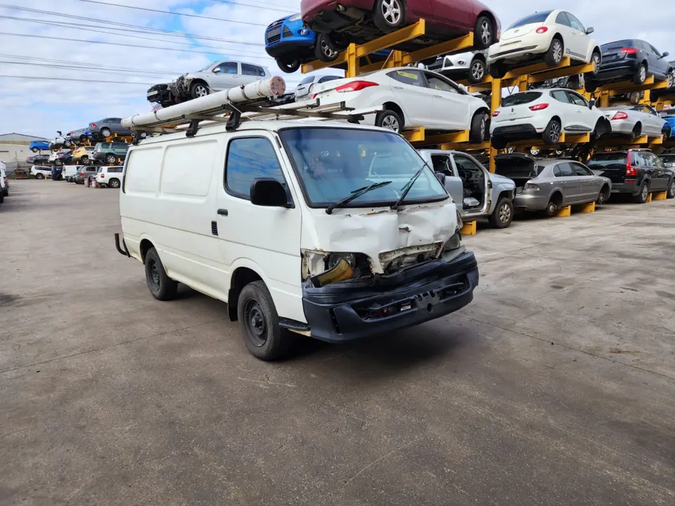 White van parked beside dismantling-yard vehicles